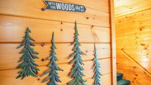 A wooden wall with a sign that reads "Into the Woods We Go" and three tree decorations.