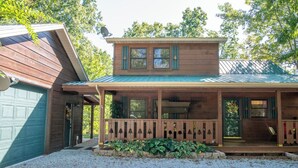 A wooden cabin with a covered porch, a garage, and a gravel driveway.