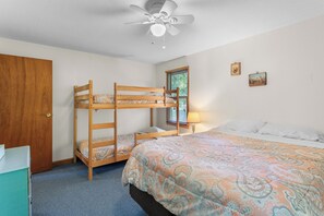 A room with bunk beds, a ceiling fan, a window with blinds, and a bed with a patterned bedspread.