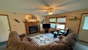 A living room with a fireplace, a ceiling fan, a television, and a sign that reads 'LAKE HOUSE'. - Charming 3-bedroom house with AC and WiFi on Sandy Pond. (Sandy Creek)