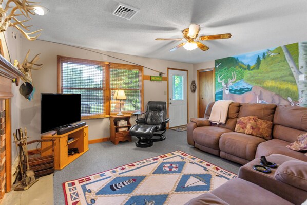 A living room with a television, a fireplace, a painting, and a ceiling fan.