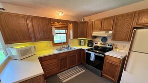 A kitchen with wooden cabinets, a microwave, a sink, a stove, and a refrigerator. - Charming 3-bedroom house with AC and WiFi on Sandy Pond. (Sandy Creek)