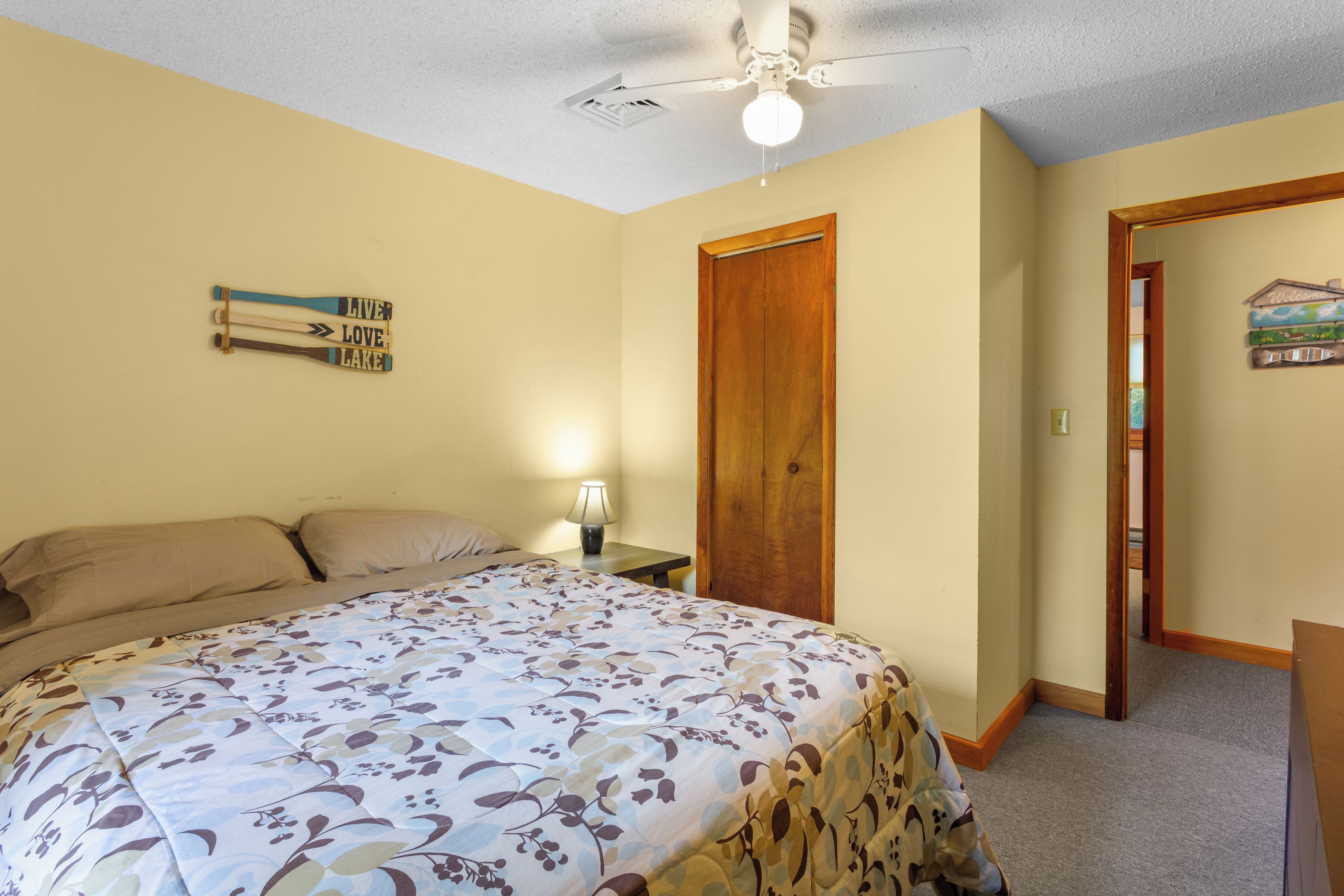 Une chambre à coucher avec un lit, une table de chevet, une lampe, un ventilateur de plafond et une porte.