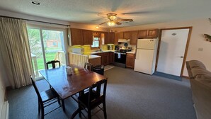 A kitchen with wooden cabinets, a dining table with chairs, a ceiling fan, and a refrigerator. - Charming 3-bedroom house with AC and WiFi on Sandy Pond. (Sandy Creek)