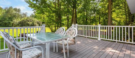 A deck with a glass-top table and chairs, surrounded by a white railing.