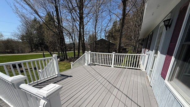 A wooden deck with white railings, a grassy yard, and trees in the background. - Charming 3-bedroom house with AC and WiFi on Sandy Pond. (Sandy Creek)