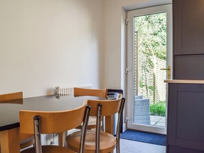 Un espace repas comprenant une table et des chaises, un radiateur et une porte donnant sur un espace extérieur avec vue sur la verdure.