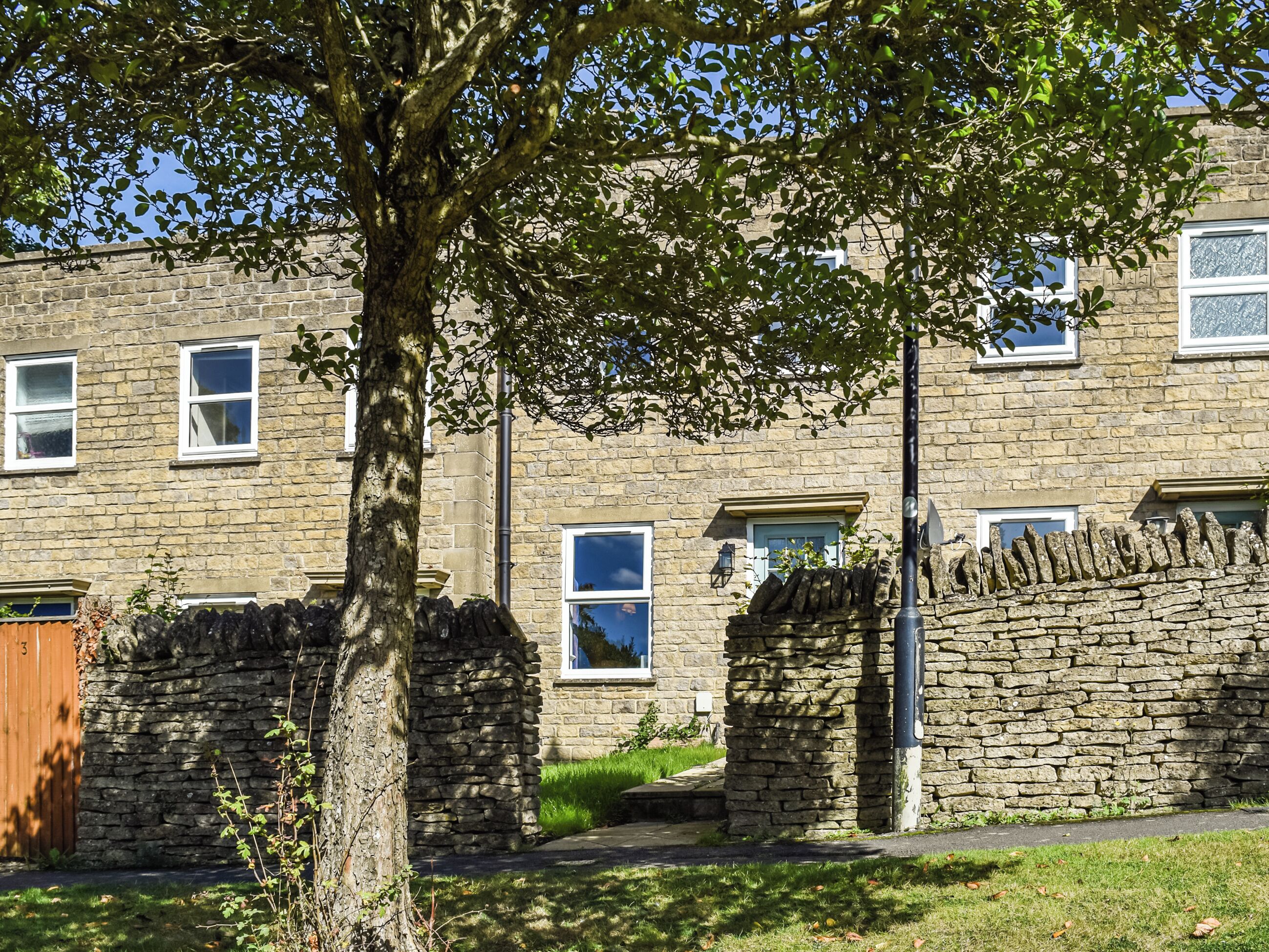 A stone building with multiple windows, a tree in the foreground, and a stone wall.