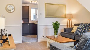 A living room with a sofa, a coffee table, a lamp, a mirror, and a clock. - The Cottage on the Green - UK47990 (Chipping Norton)