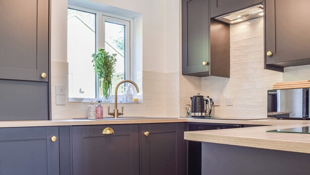 A modern kitchen with dark cabinetry, a window with a view, a coffee maker, and a microwave. - The Cottage on the Green - UK47990 (Chipping Norton)