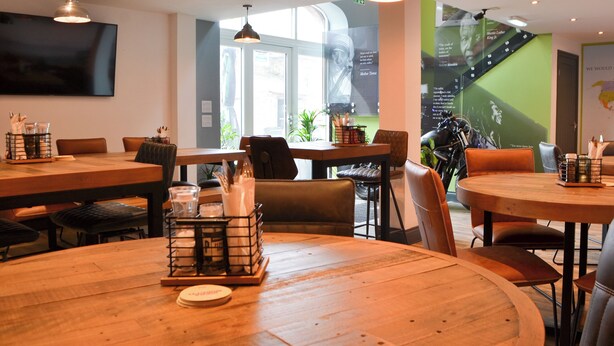 Un comedor moderno con mesas y sillas de madera, iluminación colgante y un amplio ventanal que proporciona luz natural.