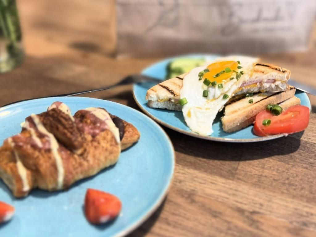 Una mesa con dos platos de comida, uno con un sándwich y un huevo, y otro con cruasanes y tomates.
