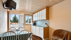 A compact kitchen with white cabinets, a dining area with a table and chairs, and a wicker sofa. - 4 Person Holiday Park Home in Graested (Graested)