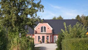 A two-story house with a dark roof and a pink facade, surrounded by greenery and a gravel path leading to the entrance. - 4 Person Holiday Park Home in Graested (Graested)