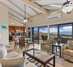 A spacious living area with a glass coffee table, comfortable seating, a ceiling fan, and a view of the ocean. - Experience paradise at Wailea Ekolu 104 with ocean views and Maui sunsets (Kihei)