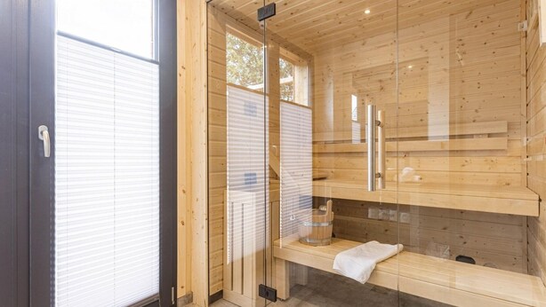 A modern sauna room with wooden walls and a glass door, featuring a bench and a towel rack. - Penthouse With Sauna (Sankt Georgen am Kreischberg)