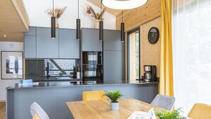 A modern kitchen with a central island, pendant lights, and a dining area with yellow chairs and a wooden table. - Penthouse With Sauna (Sankt Georgen am Kreischberg)