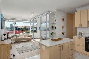 A modern kitchen with a large window, a dining area with a sofa, and a view of the cityscape. - Modern Apartment in Vibrant Green Point (Cape Town)
