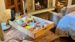 Ein gemütliches Zimmer mit Kamin aus Stein, einem darüber hängenden Fernseher und einem Frühstücksbrett auf dem Tisch.