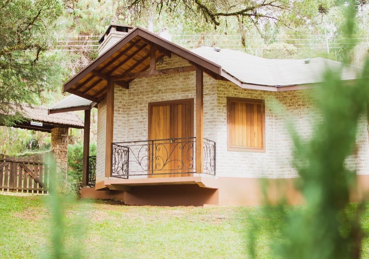 A rustic stone building with a wooden door and windows, a covered porch, and a fenced yard.