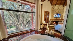 Ein Zimmer mit einer großen Badewanne, einem Kamin aus Stein und einem an der Wand befestigten Fernseher.