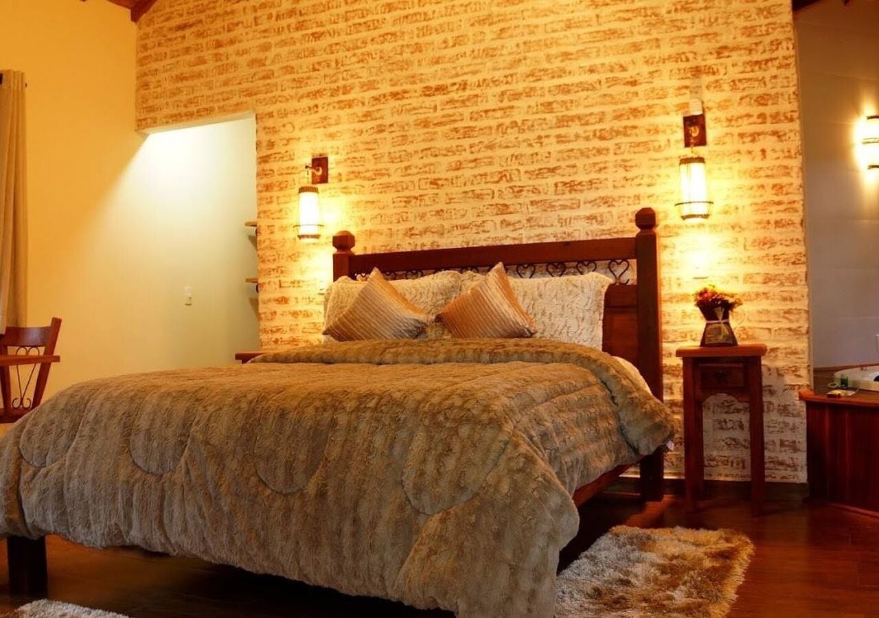 Une chambre à coucher avec un grand lit, une tête de lit en bois, deux lampes fixées au mur et un mur décoré d’un motif en briques.
