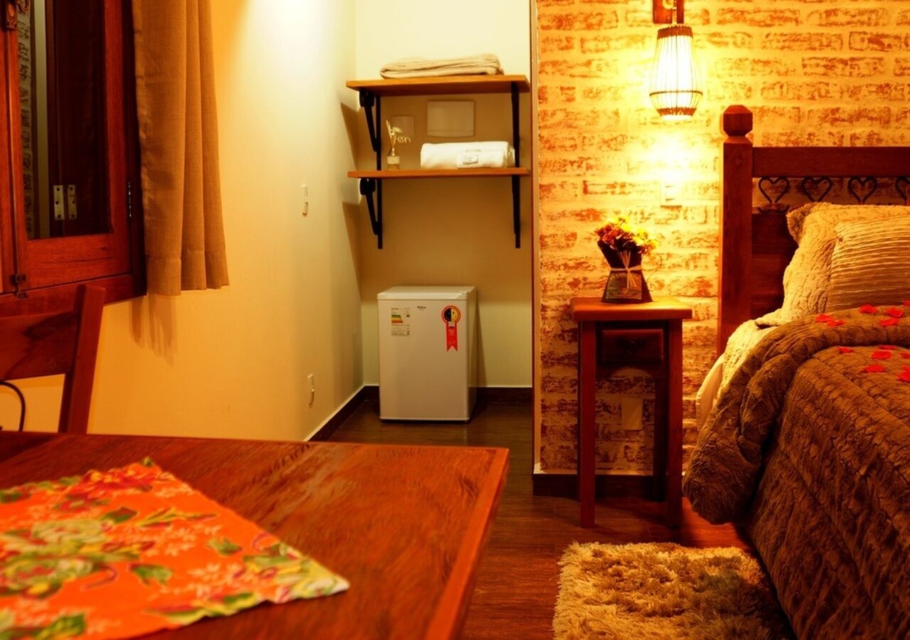 Una habitación acogedora con una cama de madera, una mesita con mantel floreado, un refrigerador y un estante con toallas.