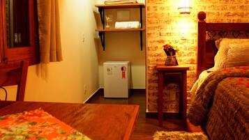Una habitación acogedora con una cama de madera, una mesita con mantel floreado, un refrigerador y un estante con toallas.