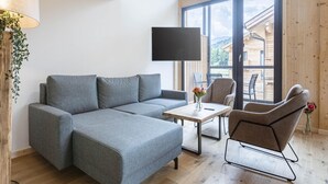 A modern living room with a grey sectional sofa, a small table with a vase of flowers, and a TV mounted on the wall. - Attractive Penthouse With Sauna (Sankt Georgen am Kreischberg)