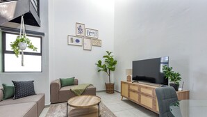A modern living room with a sofa, armchair, round coffee table, TV, and potted plants.