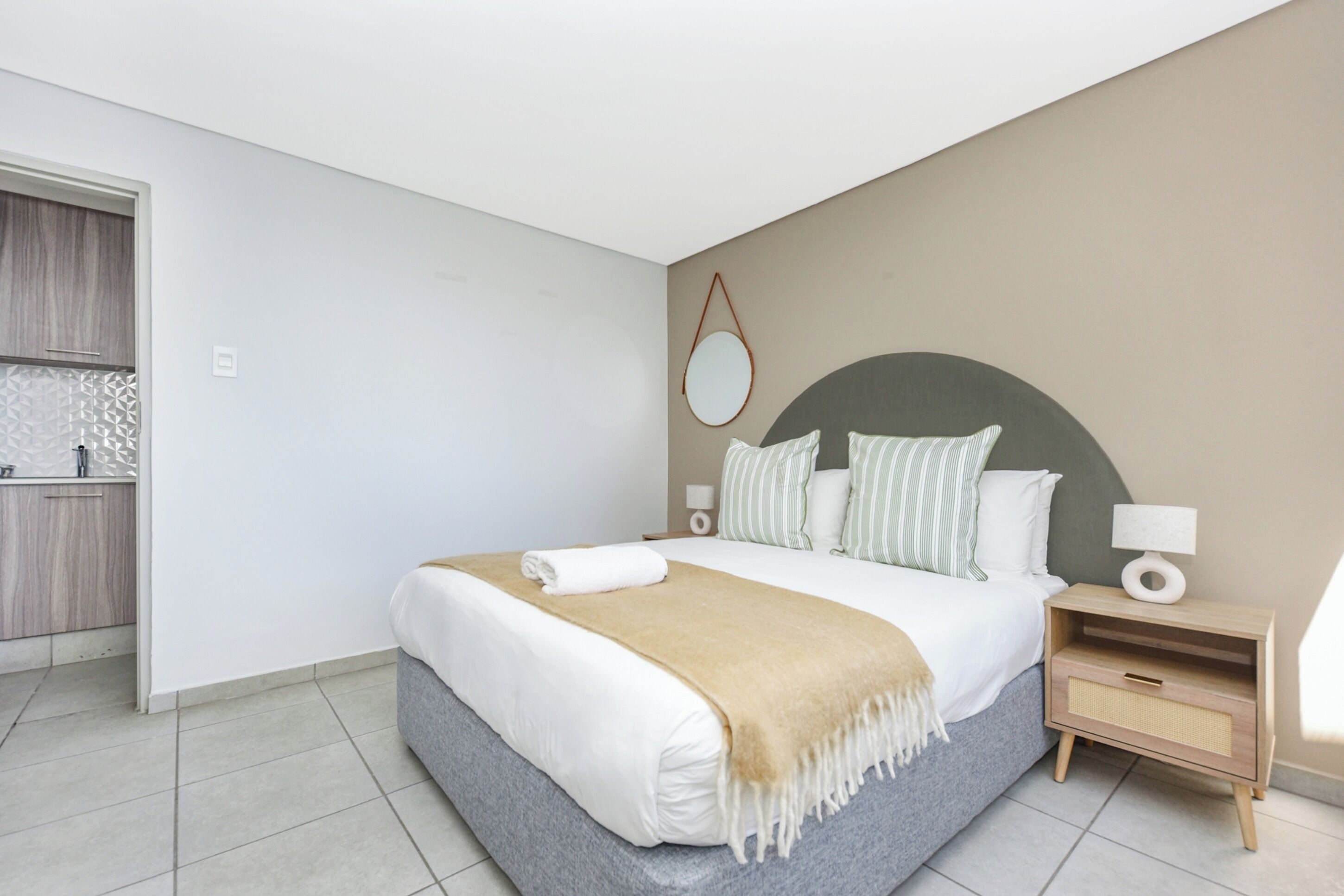 A modern bedroom with a large bed, bedside tables, a nightstand, and a wall-mounted mirror.