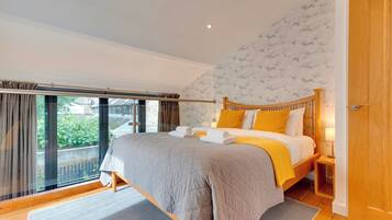A bedroom with a large bed, a wooden headboard, a nightstand, and a view of greenery outside.