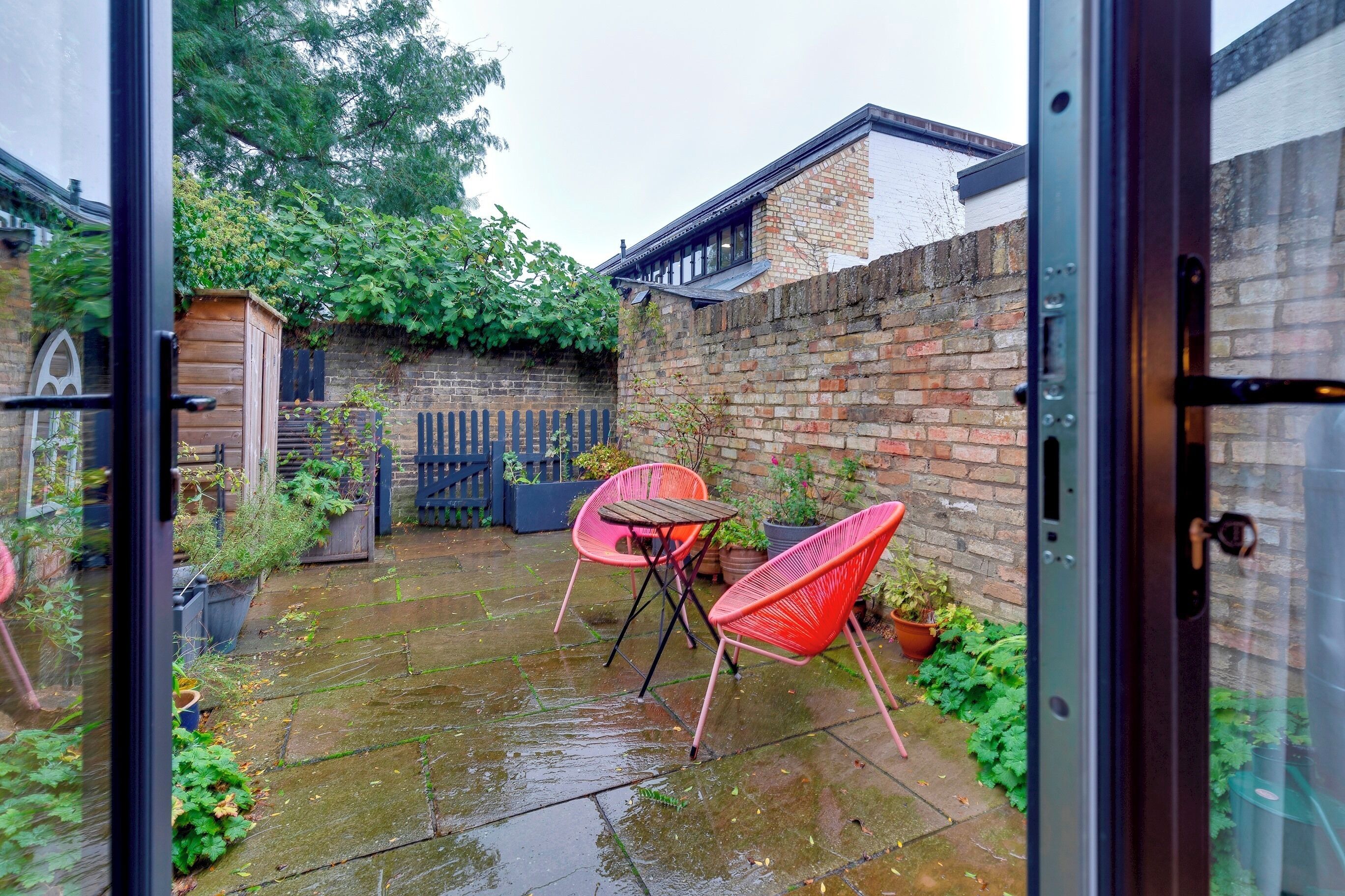 A wet patio with two red chairs and a table, surrounded by brick walls and greenery.