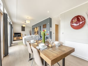 A dining area with a wooden table set for four, a sofa in the background, and a red abstract art piece on the wall.