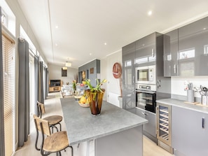 A modern kitchen with grey cabinets, a central island with seating, and a dining area with a TV.