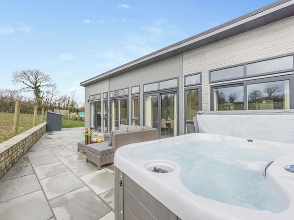 A modern outdoor patio with a hot tub, wicker furniture, and a glass-enclosed patio area.