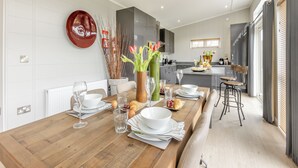 A modern kitchen with a dining area, featuring a wooden table set for a meal, a vase with flowers, and a view of the kitchen in the background. - 2 bedroom accommodation in Roadford Lake, near Launceston (Roadford Lake, near Launceston)