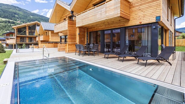 A wooden cabin with a pool, outdoor seating, and a mountain backdrop. - Amazing Penthouse With Sauna (Sankt Georgen am Kreischberg)