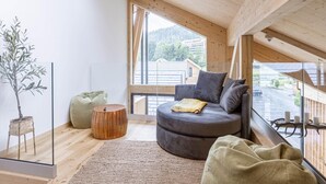 A modern loft bedroom with a sloped ceiling, large windows, a grey sofa, a round wooden stool, and a green pouf. - Amazing Penthouse With Sauna (Sankt Georgen am Kreischberg)