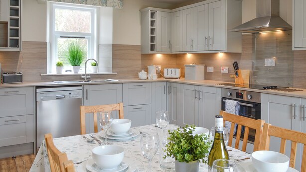 A modern kitchen with white cabinetry, a built-in oven, and a dining area set for four with a table set for a meal. - 3 bedroom accommodation in Arbroath (Arbroath)