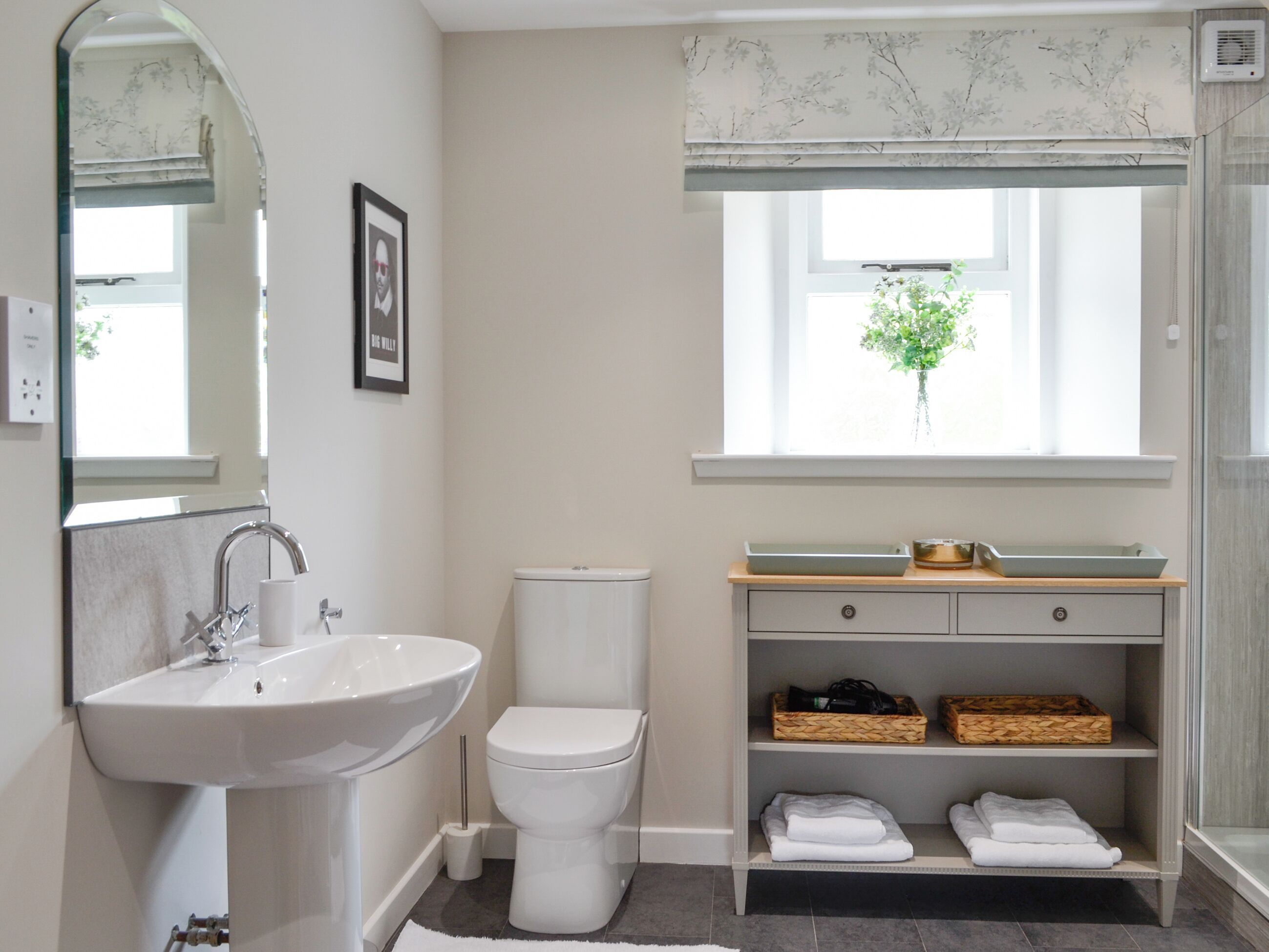 Een moderne badkamer met een wastafel, toilet en een badkamermeubel. Er is een raam met uitzicht op groen.