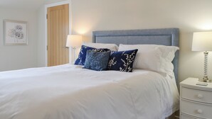 A neatly made bed with white linens, a blue headboard, and decorative pillows. There is a bedside table with a lamp and a framed picture on the wall. - 3 bedroom accommodation in Arbroath (Arbroath)