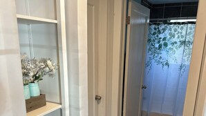 Un couloir avec une porte blanche donnant sur une salle de bain équipée d’un rideau de douche.