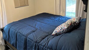 Une chambre à coucher avec un lit, une fenêtre avec des rideaux et un mur orné d’un motif géométrique.