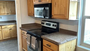 Une cuisine avec des meubles de rangement en bois, une cuisinière en acier inoxydable, un four à micro-ondes et une poubelle.