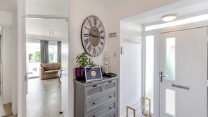 A hallway with a large wall clock, a small table with a potted plant, and a door with a frosted glass window.