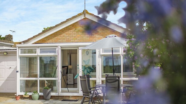 A house with a conservatory, a patio with a table and chairs, and a garden.