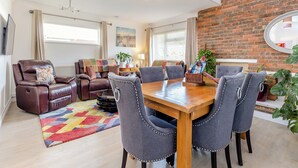 A modern living room with a leather sofa, a dining table with six chairs, a colorful rug, and a brick wall.