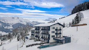 A modern multi-story hotel with balconies, a swimming pool, and a view of snow-covered mountains. - Nice Apartment With Shared Pool (Sankt Martin am Tennengebirge)