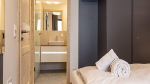 A hotel room with a wooden door, a bed with white linens, a dark wall, and a mirror above the sink. - Nice Apartment With Shared Pool (Sankt Martin am Tennengebirge)